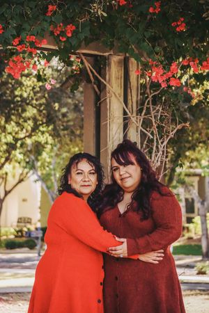 Two people in red sweaters posing under trees with red berries.