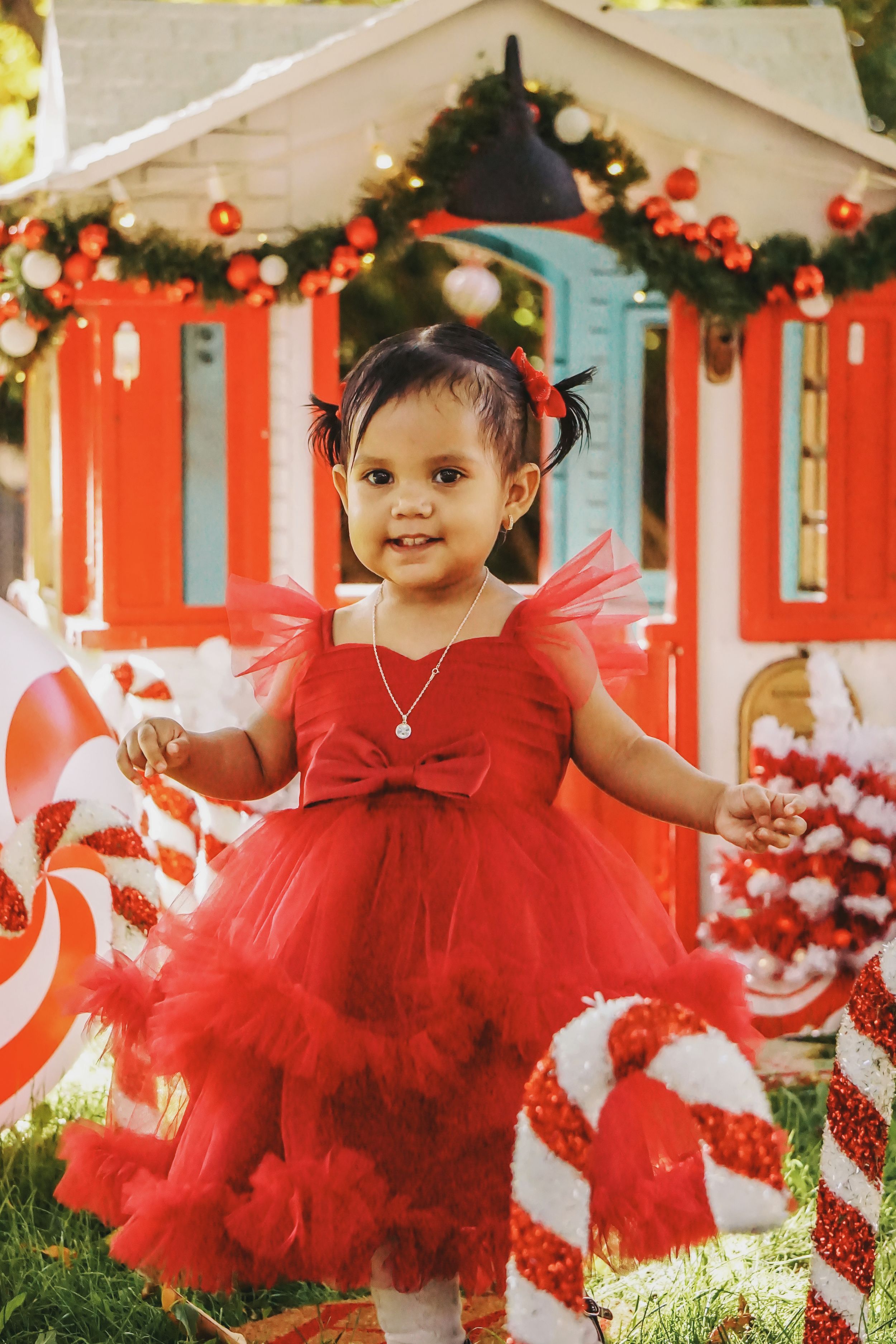 Child wearing a festive red tulle dress posing in front of holiday decorations.