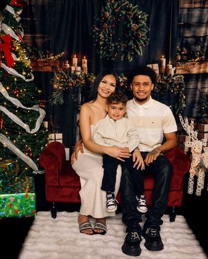Family photo session with matching white outfits on red velvet couch with holiday decorations.