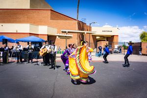 People gathered in a parking lot on a sunny day with buildings in background.