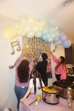 Celebration scene with pastel balloon arch and people dancing under decorative lighting.