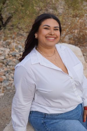 Woman in white button-up shirt and jeans posing outdoors.