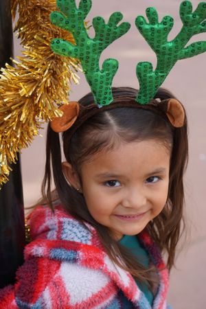 Child wearing festive cactus headband with gold tinsel decorations.