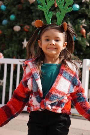 Child wearing festive reindeer antlers and plaid jacket during holiday season.
