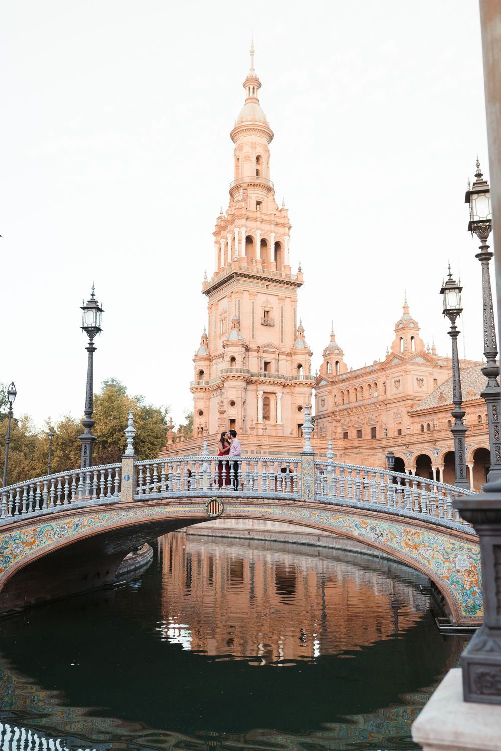 Beautiful bridge with ceramic tiles spans water at Plaza de España in Seville at sunset.