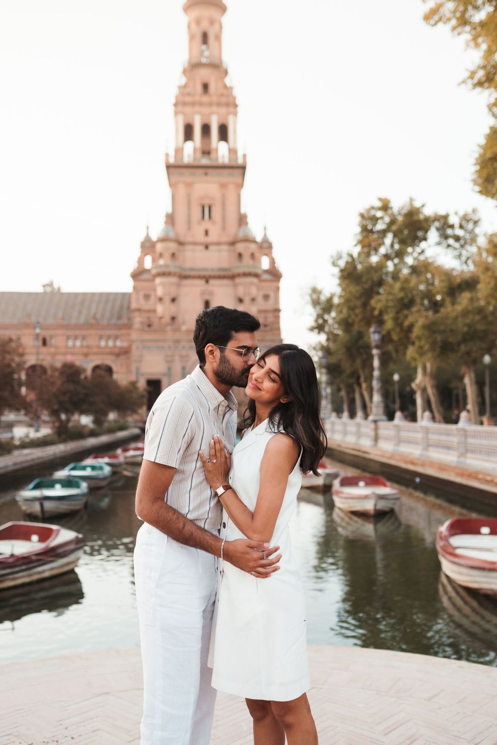 A romantic moment by the canal with boats and a historic tower in Seville.