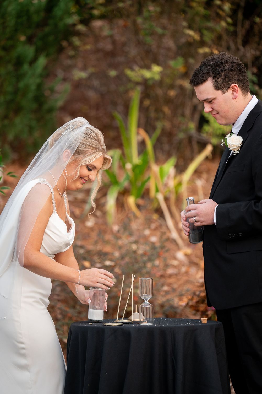 Wedding couple performs unity ceremony at black-draped table during outdoor celebration.