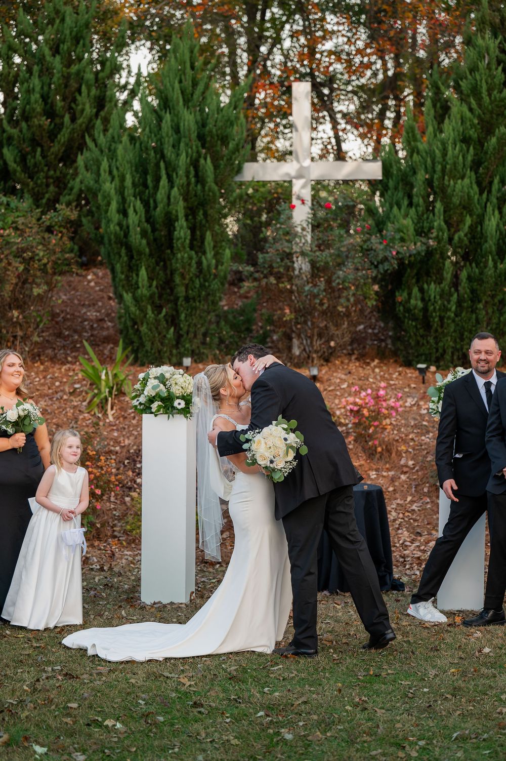 Wedding ceremony candid moments captured with white pillars and evergreen backdrop.