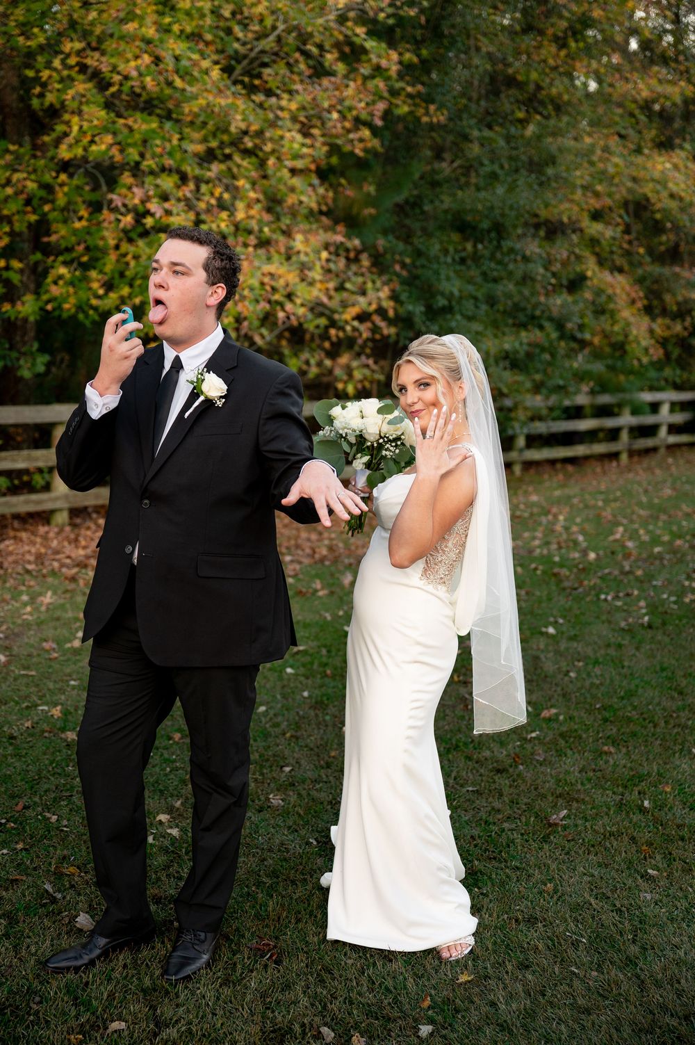 Playful wedding couple shares lighthearted moment on grassy lawn during autumn celebration.