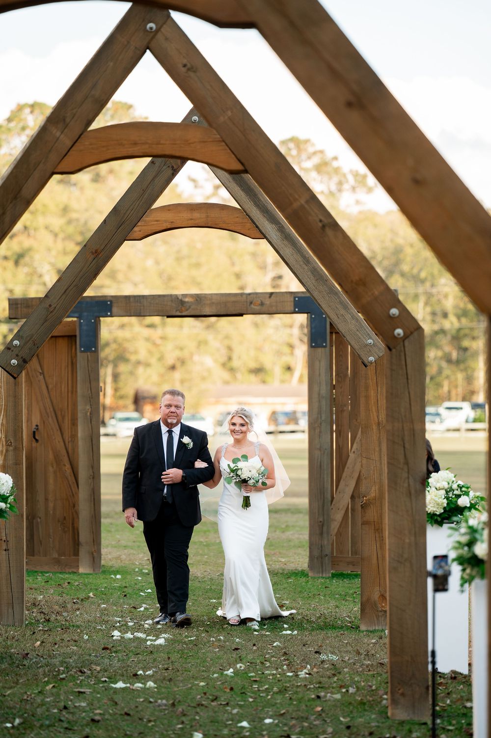 Rustic wooden archway frames wedding ceremony path with decorative floral arrangements.