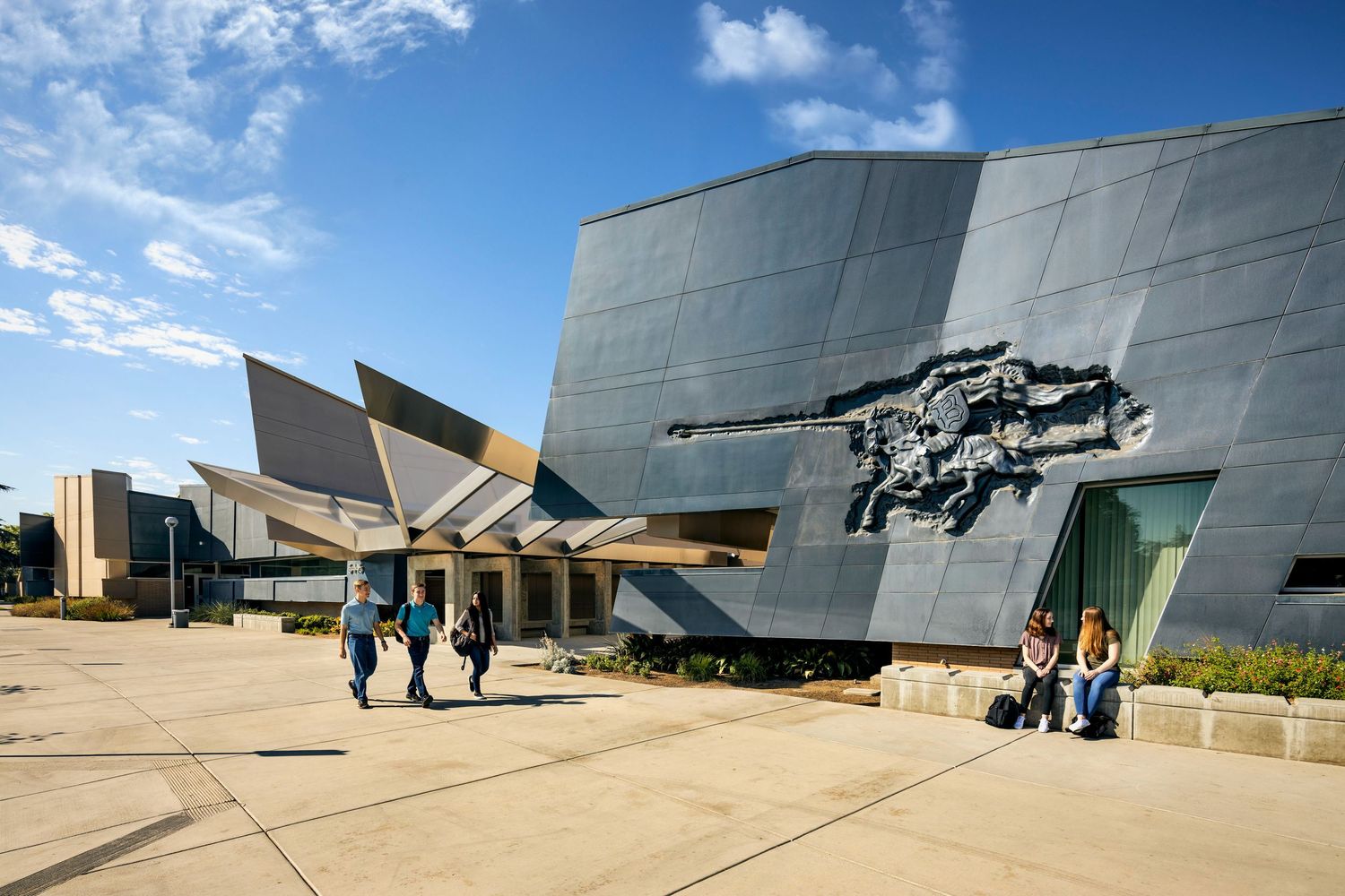 Military aircraft and helicopters displayed outside a modern aviation museum building under blue skies.