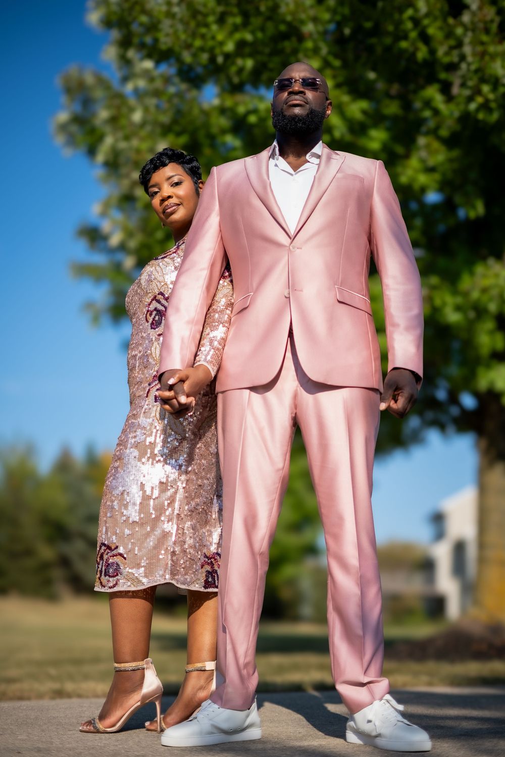 Couple in coordinating pink formal wear poses outdoors on a sunny day.