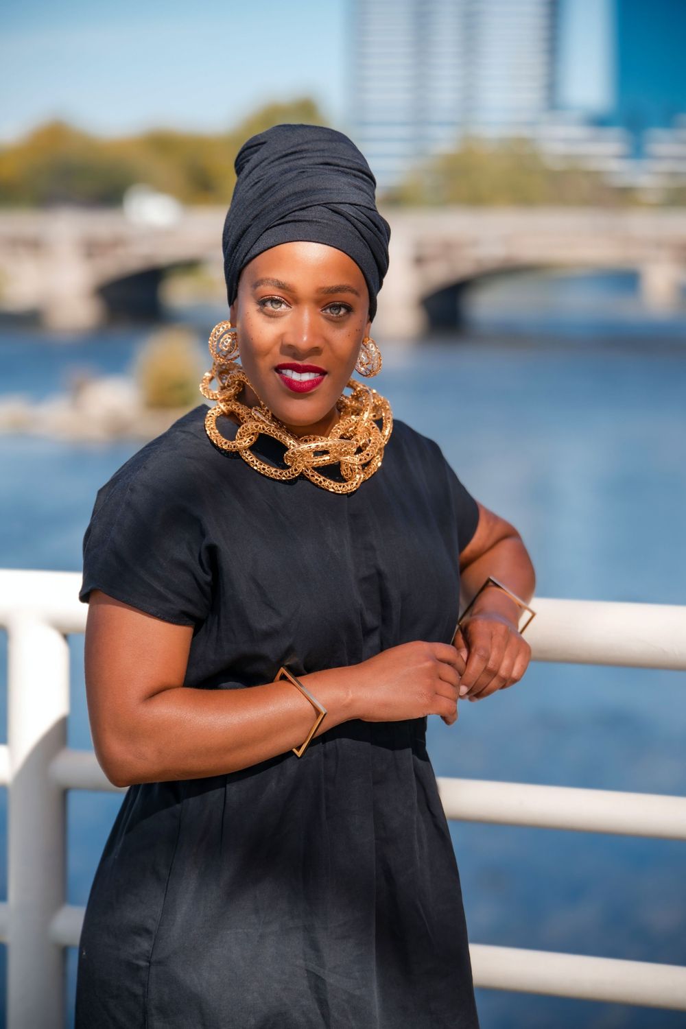 Waterfront portrait series featuring black outfit and statement gold necklace against river backdrop.