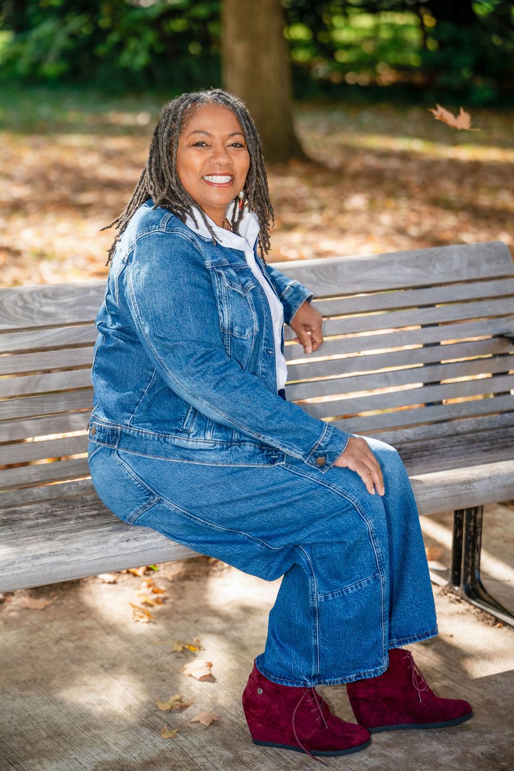 Casual outdoor portrait series on a wooden park bench featuring denim jacket and burgundy pants.