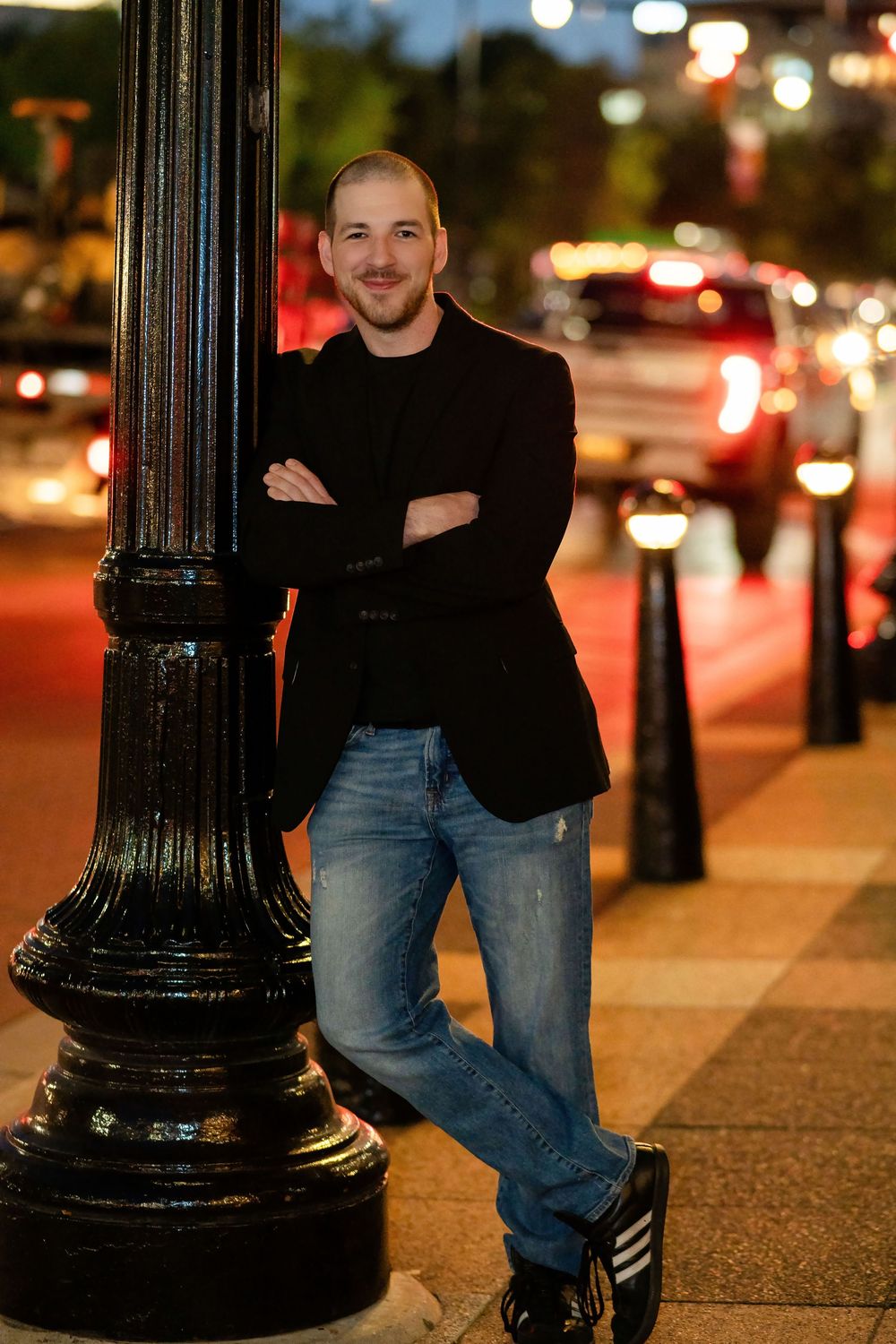Nighttime urban portrait series next to decorative black street lamp with city lights in background.