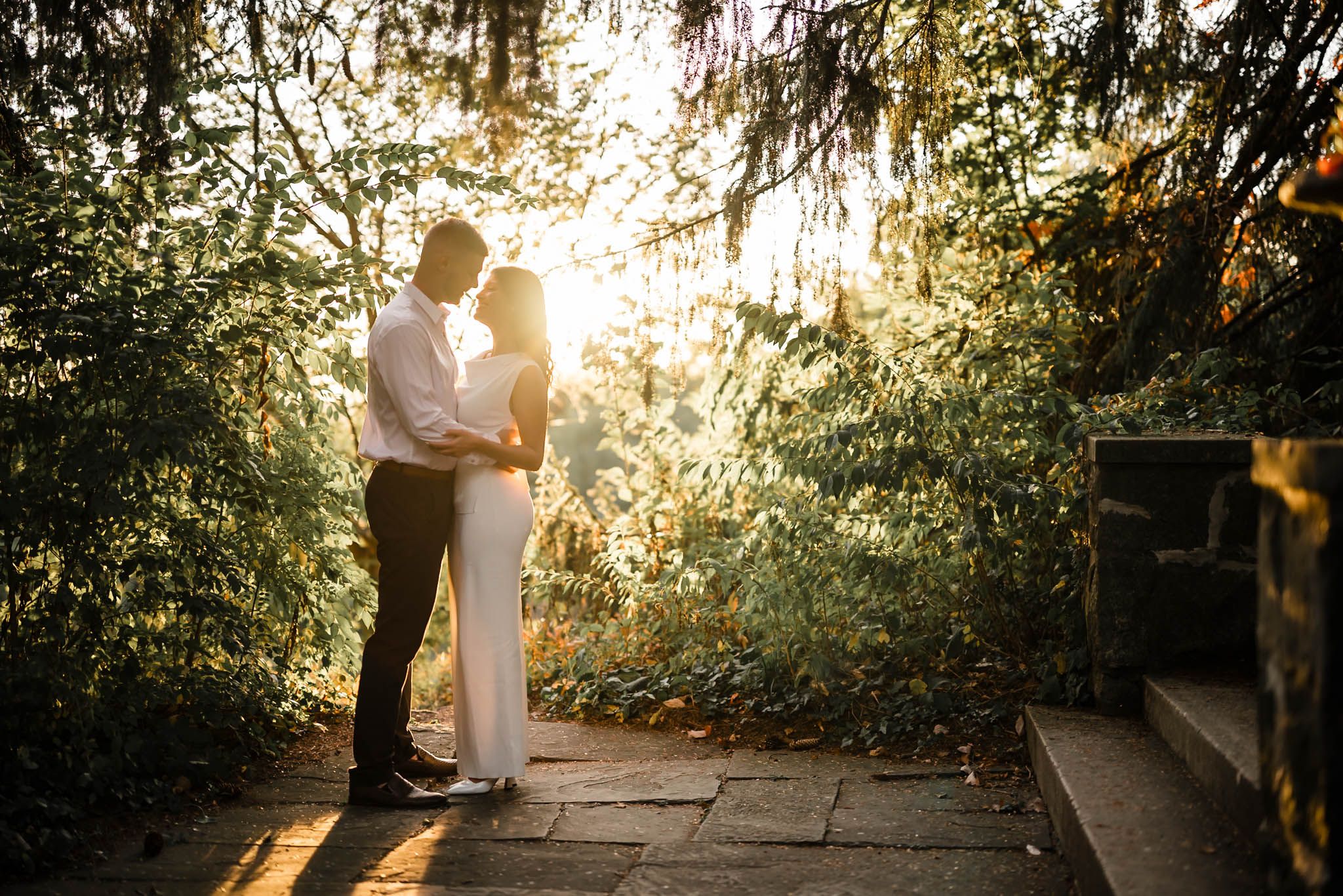 Couple shares intimate moment under tree canopy during golden hour.