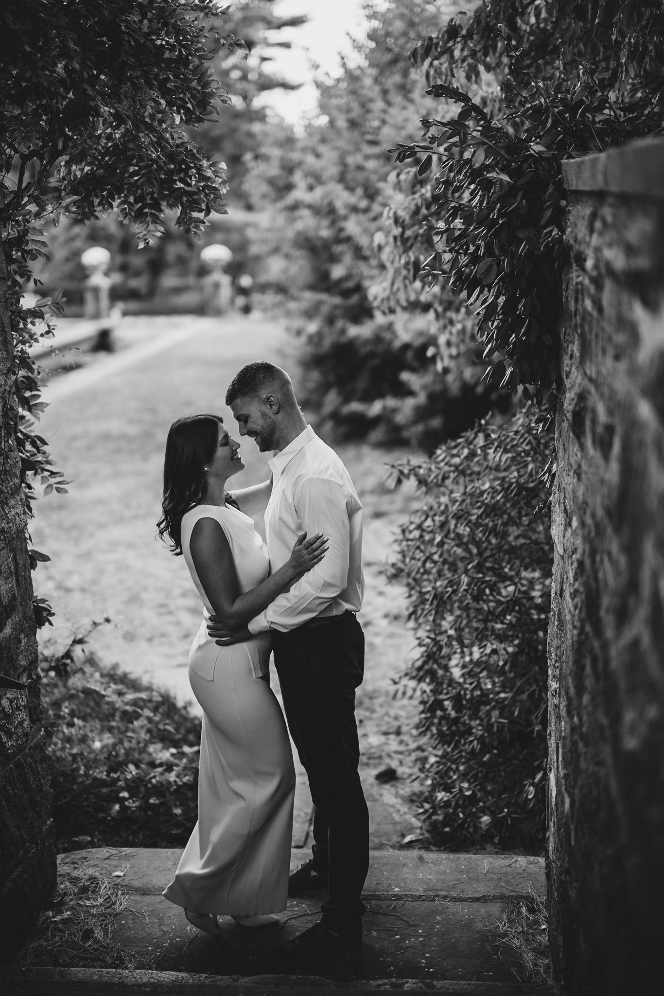 Romantic couple poses along stone pathway surrounded by lush greenery.