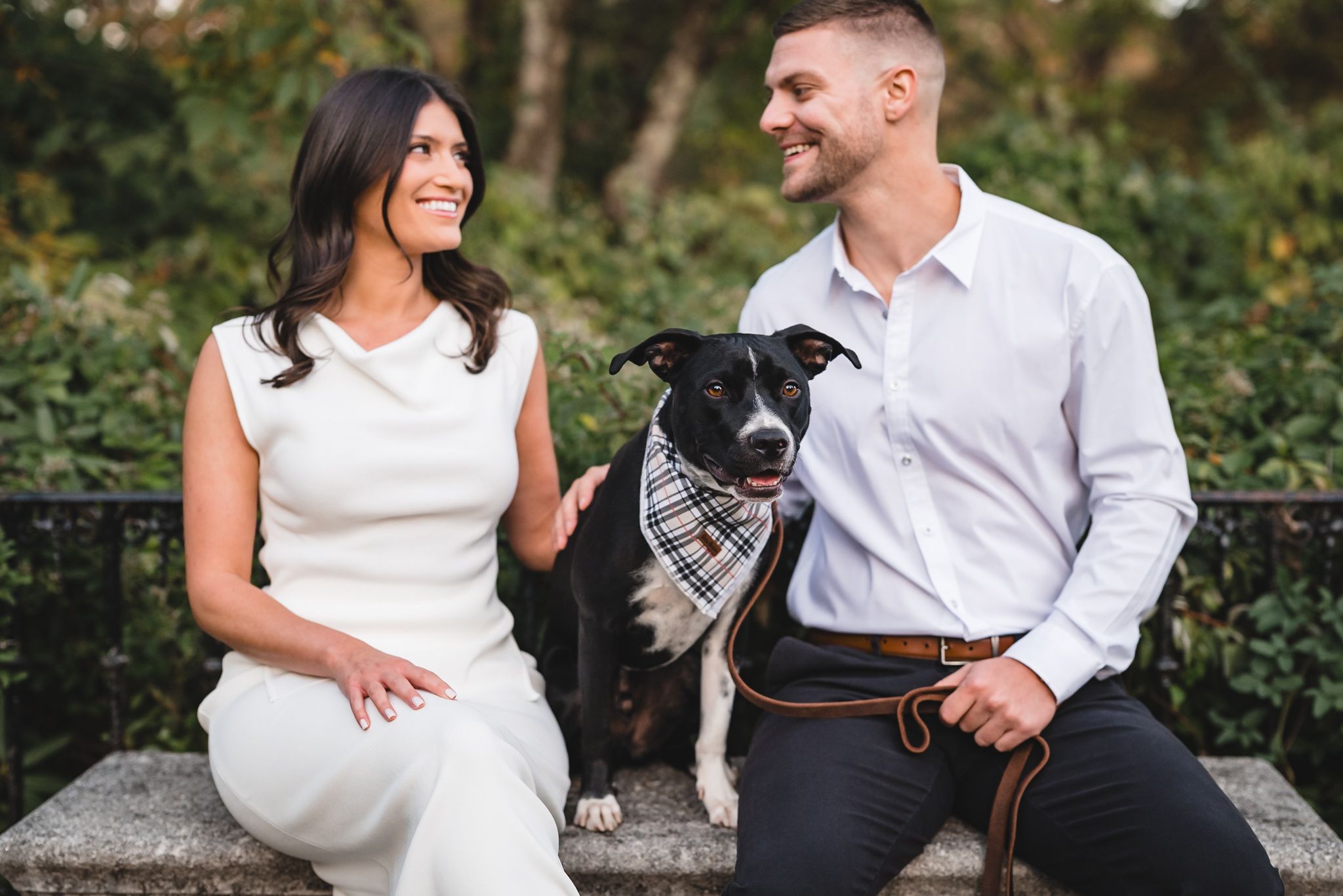 Couple relaxes on stone steps with their Boston terrier during outdoor photoshoot.