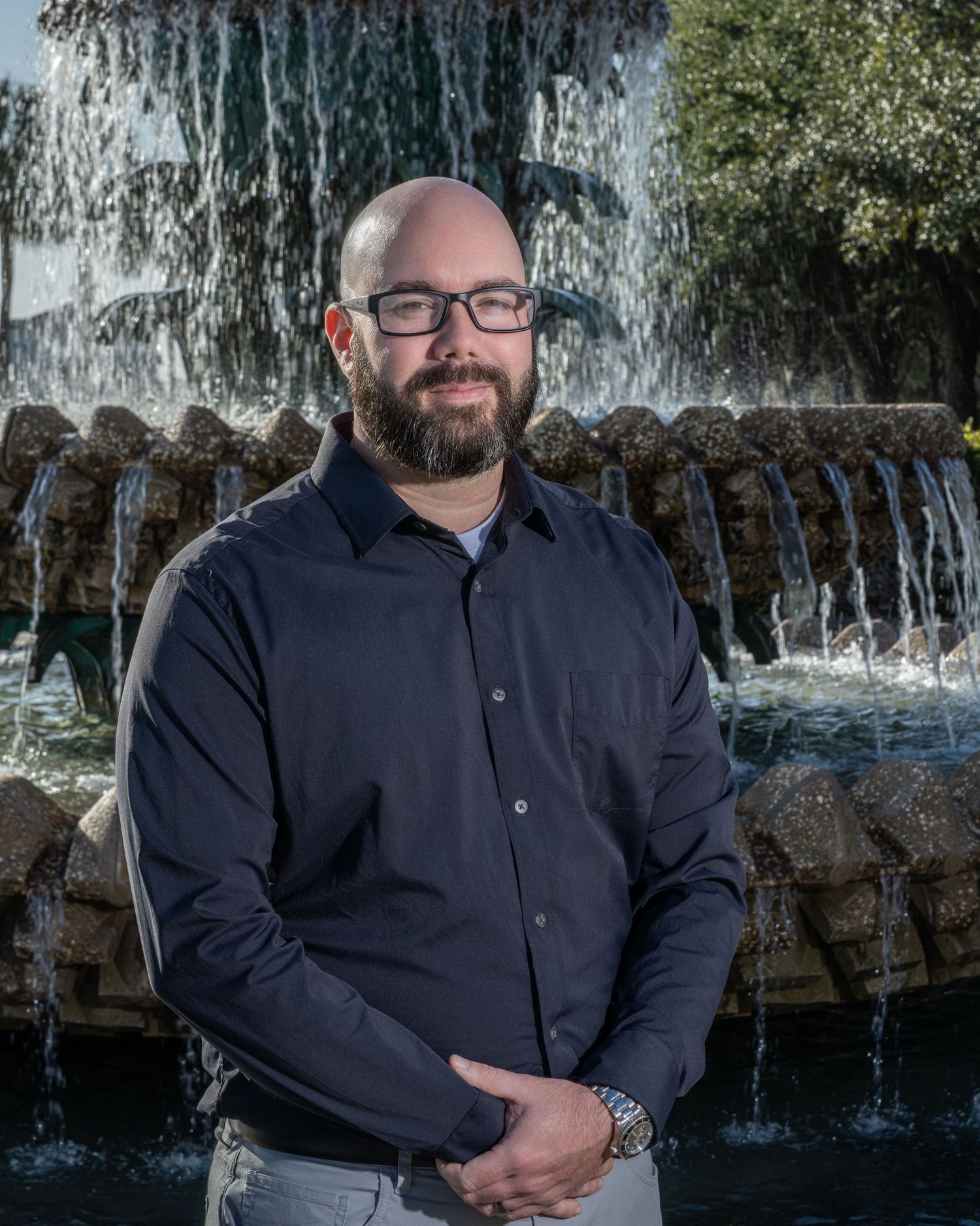 Professional portrait of a man in a dark button-down shirt standing in front of the Pineapple Fountain in Charleston, SC
