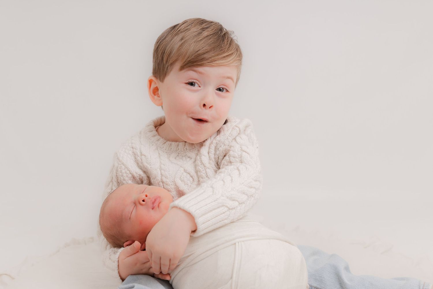 Sweet baby in cream cable knit sweater sits on white background during professional studio portrait session.
