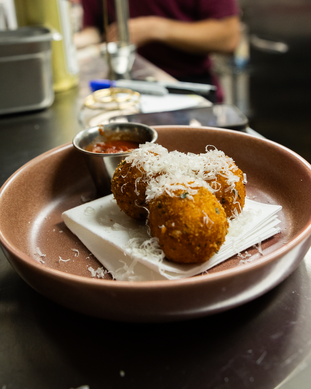 Golden fried arancini balls topped with shredded parmesan served on a brown ceramic plate with marinara dipping sauce.