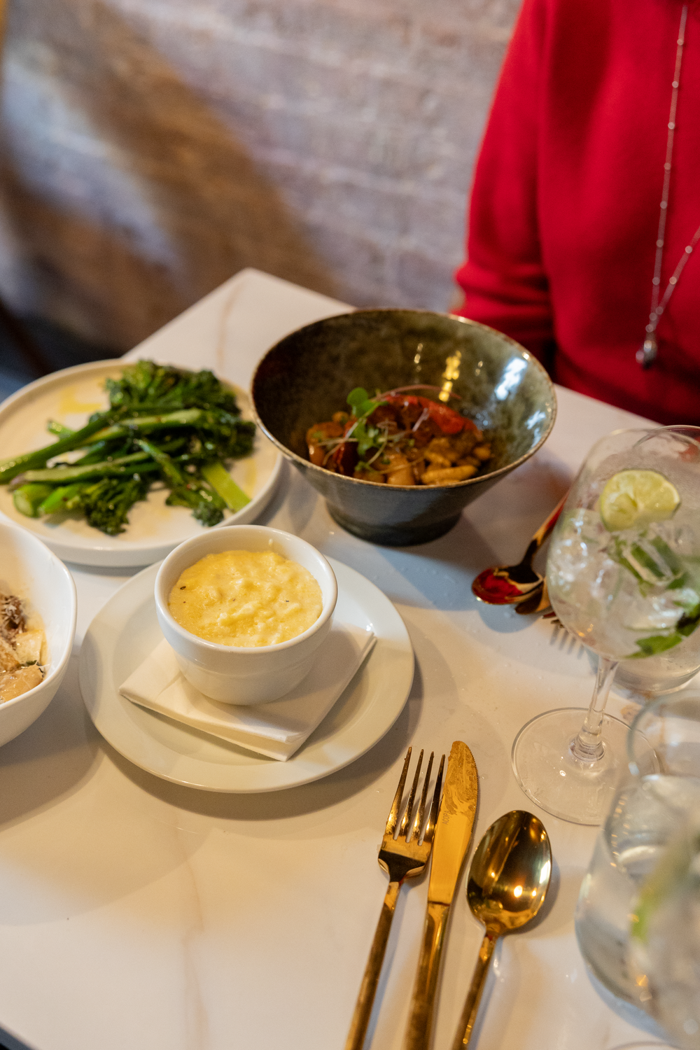 Restaurant table with multiple dishes including broccoli, pasta, soup, and sparkling water with lime.
