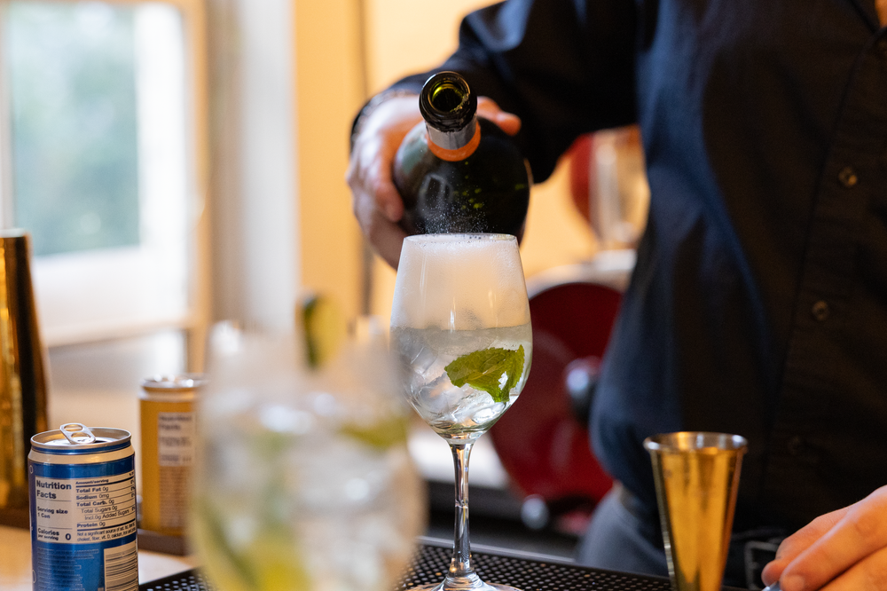 Bartender pouring sparkling beverage into wine glass with lime garnish at restaurant bar.