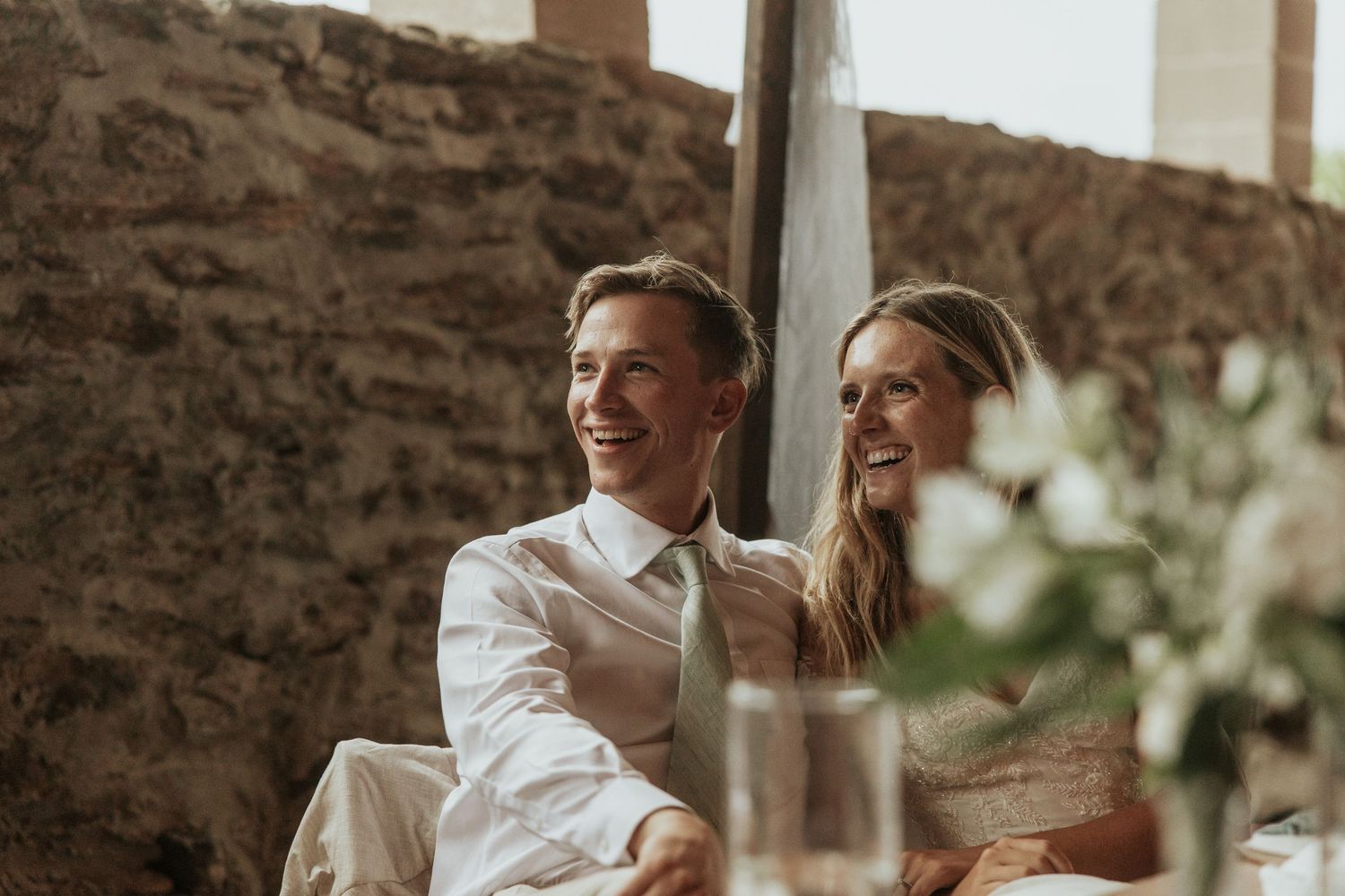 Couple shares joyful laughter during an intimate moment at a rustic stone venue.