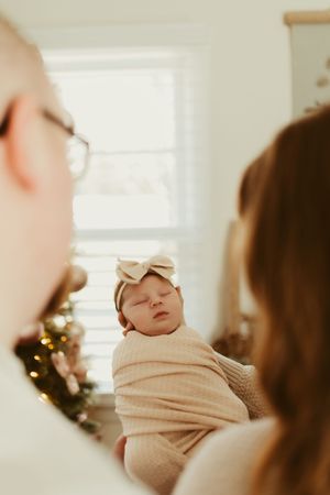 Parents gazing lovingly at their swaddled newborn baby girl wearing a cream bow headband.