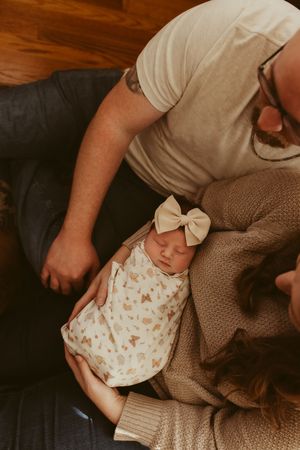 Sleeping newborn girl in butterfly print swaddle with cream bow headband resting in parents arms.