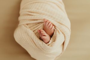Close-up of a swaddled newborn baby's tiny feet peeking out from a soft cream muslin wrap.