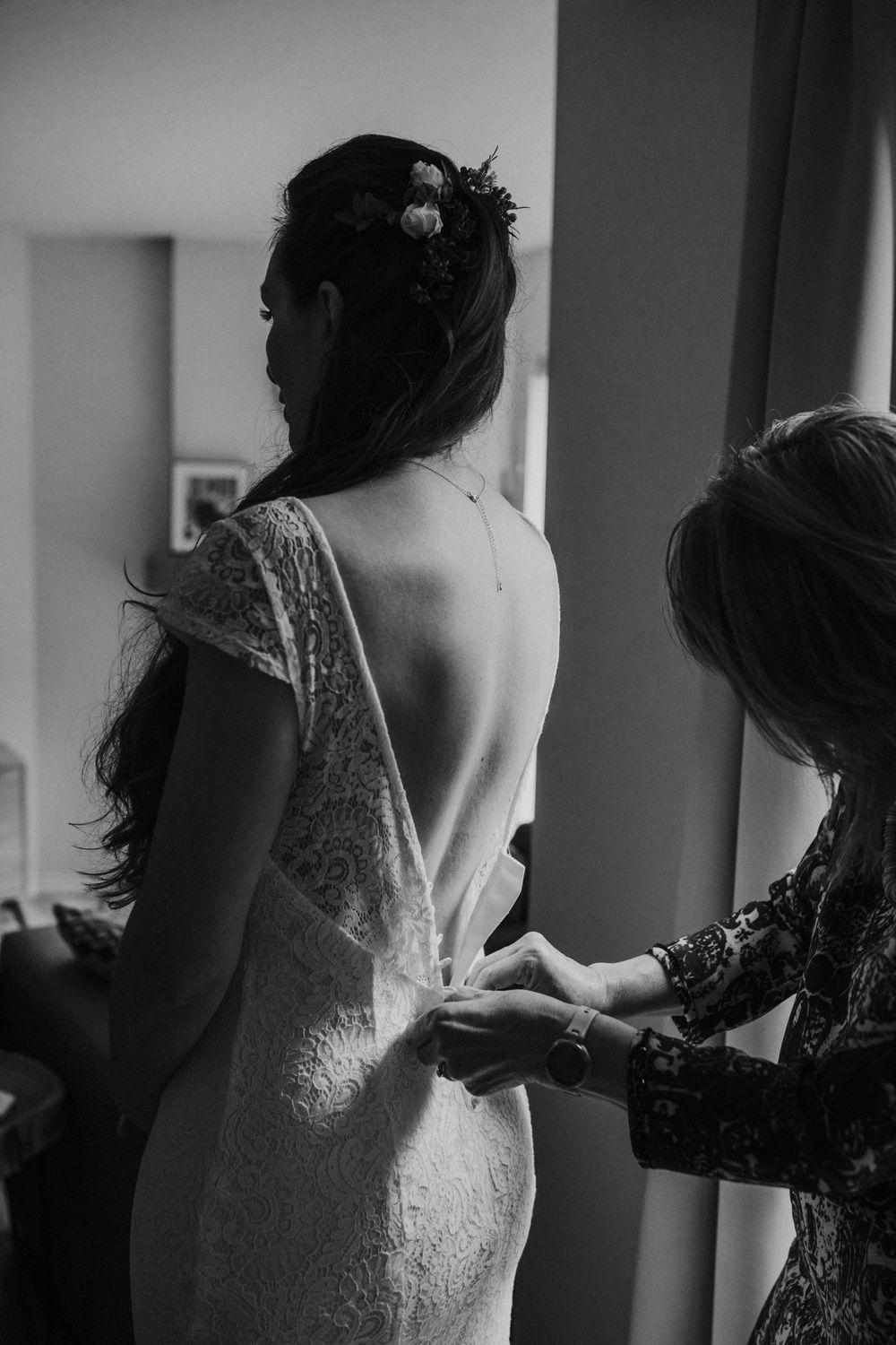 A series of silhouetted shots showing someone helping a bride get dressed in a lace wedding gown.