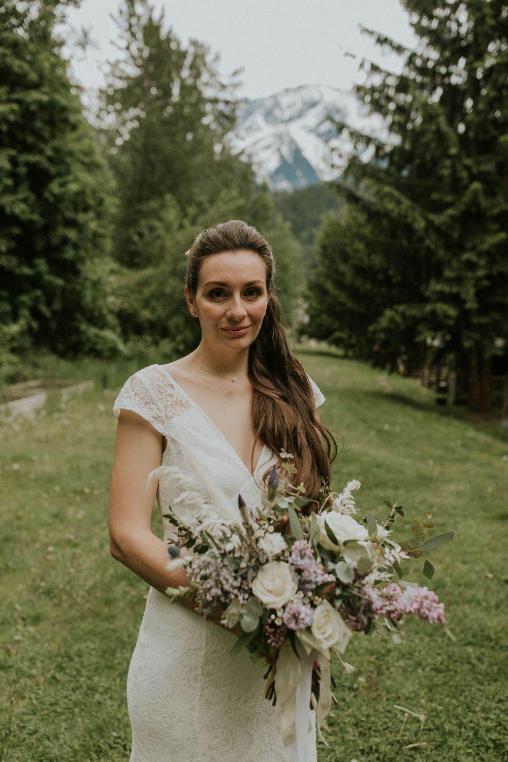 Beautiful bridal bouquet with white roses and greenery against a mountain backdrop in an outdoor setting.