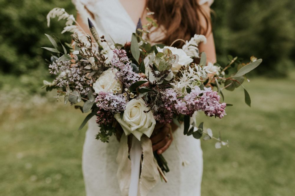A delicate bouquet of white and purple wildflowers with green foliage held against a blurred outdoor background.