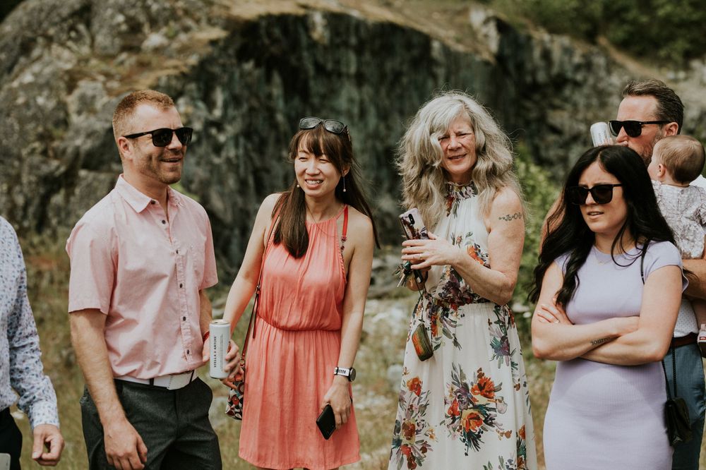 A wedding party wearing coral and white dresses poses together outdoors against a stone wall background.