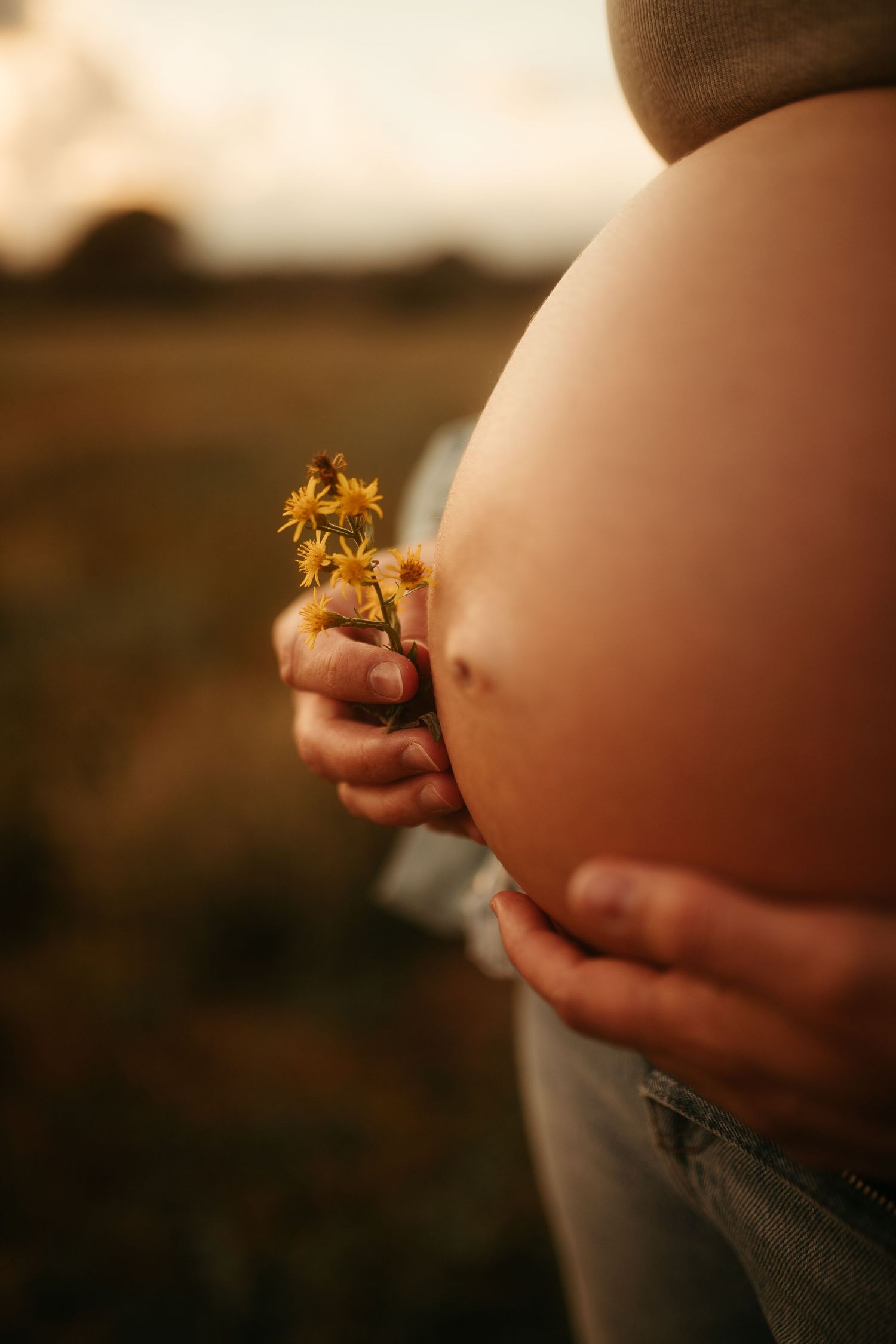 Barriga embarazada con flor en sesión de embarazo en el campo en Tarragona