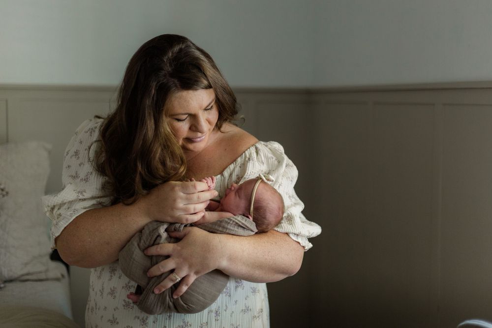 Parent holding and comforting newborn baby in soft natural light near window.
