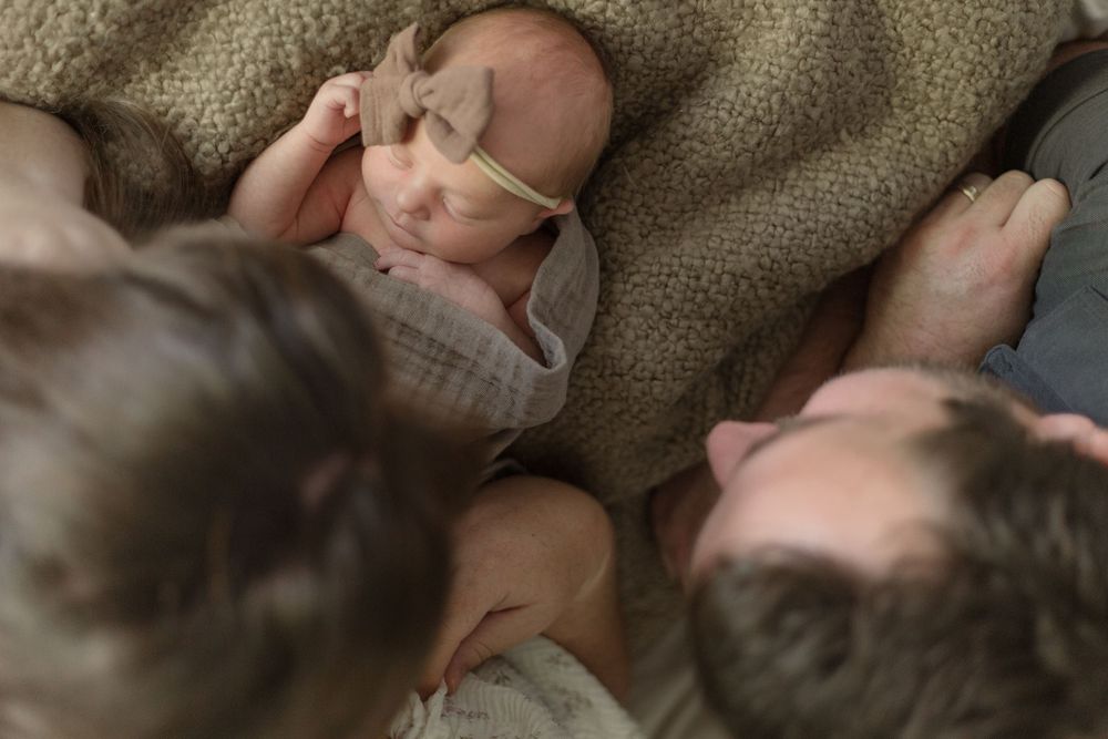 A newborn baby rests on a soft blanket while family members lovingly gaze at the peaceful scene.