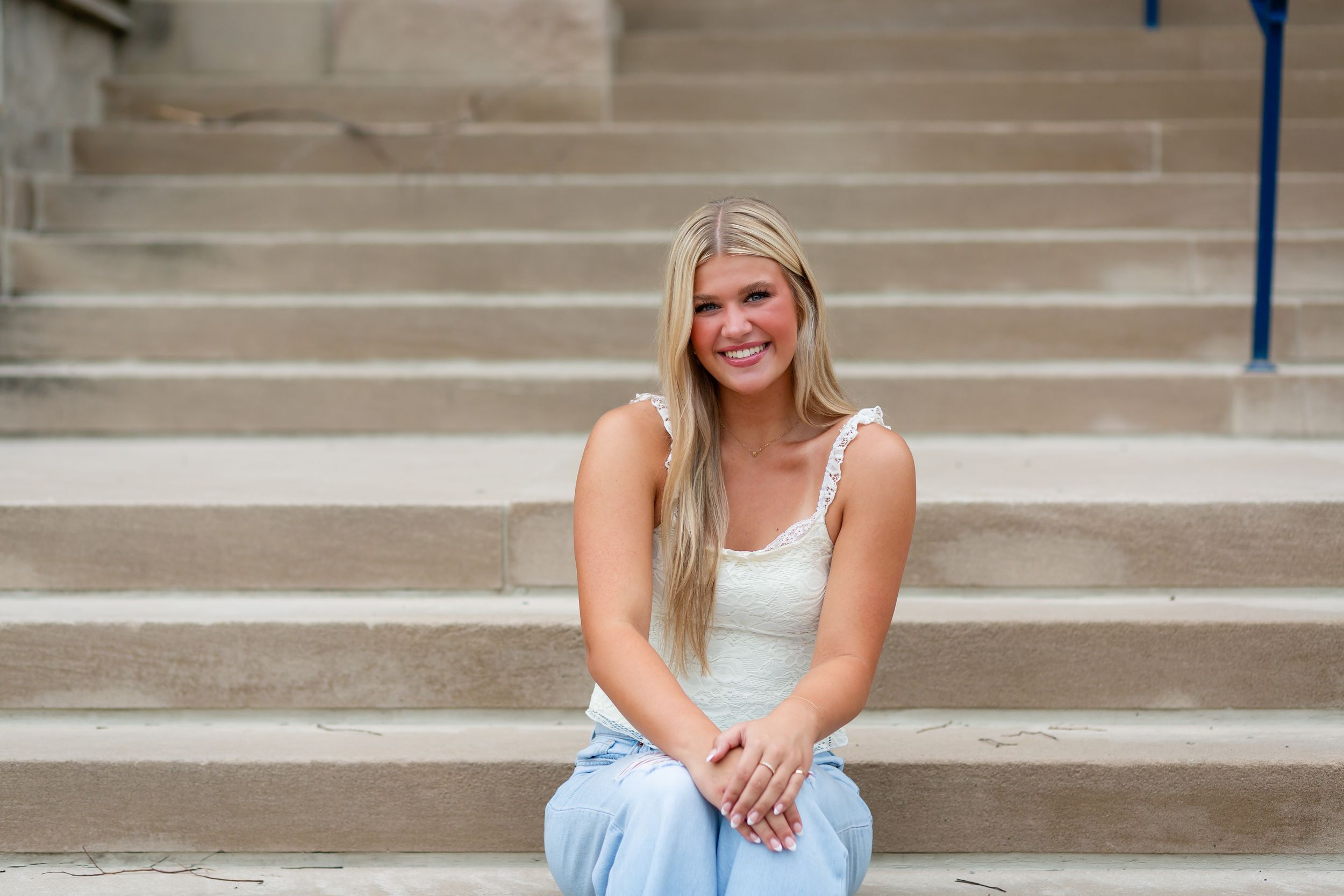 High school senior girl sitting on concrete steps in downtown Cedar Rapids, IA wearing casual denim and white top.