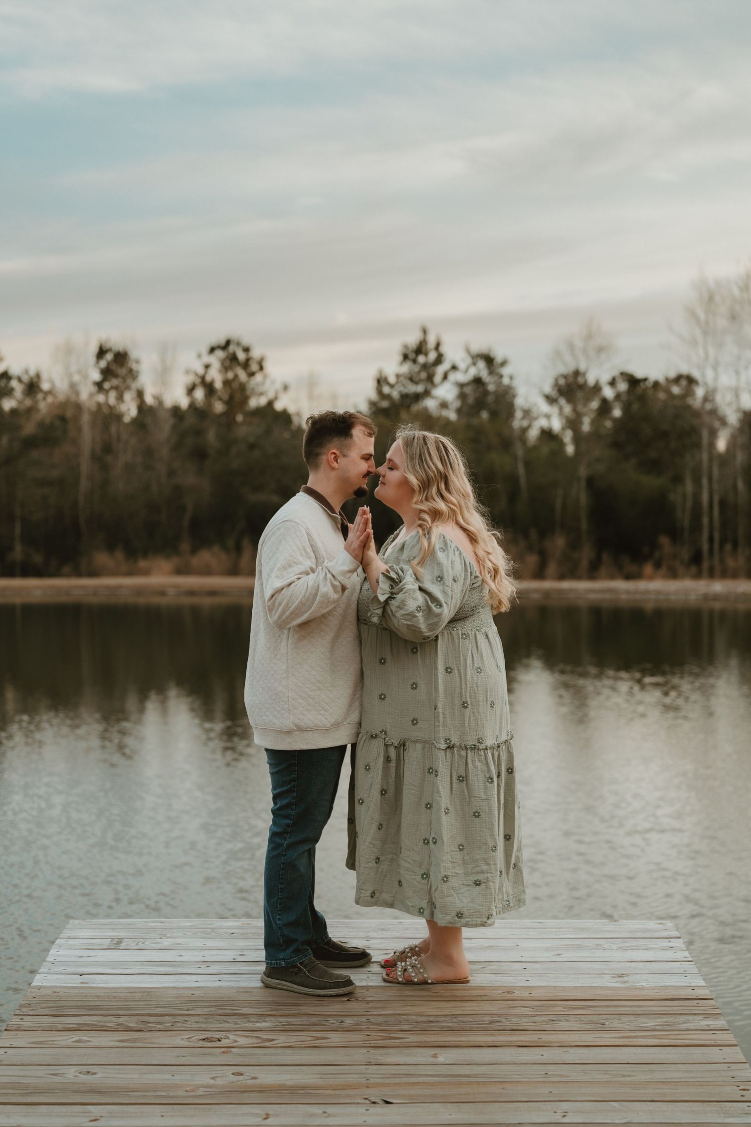 Romantic couple sharing tender moments on a wooden dock by a serene lake during sunset.