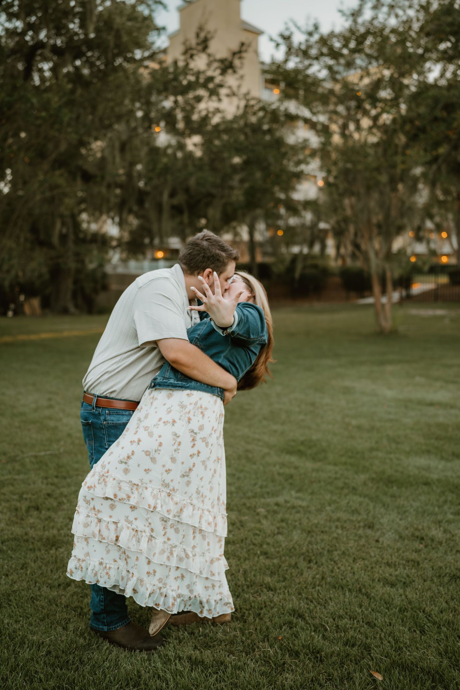 A romantic couple embraces in a dip pose on lush green grass during an outdoor photo session at sunset.
