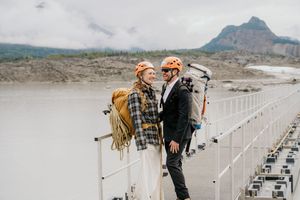 Couple in winter attire shares intimate moments on a wooden bridge with mountain views in the background.