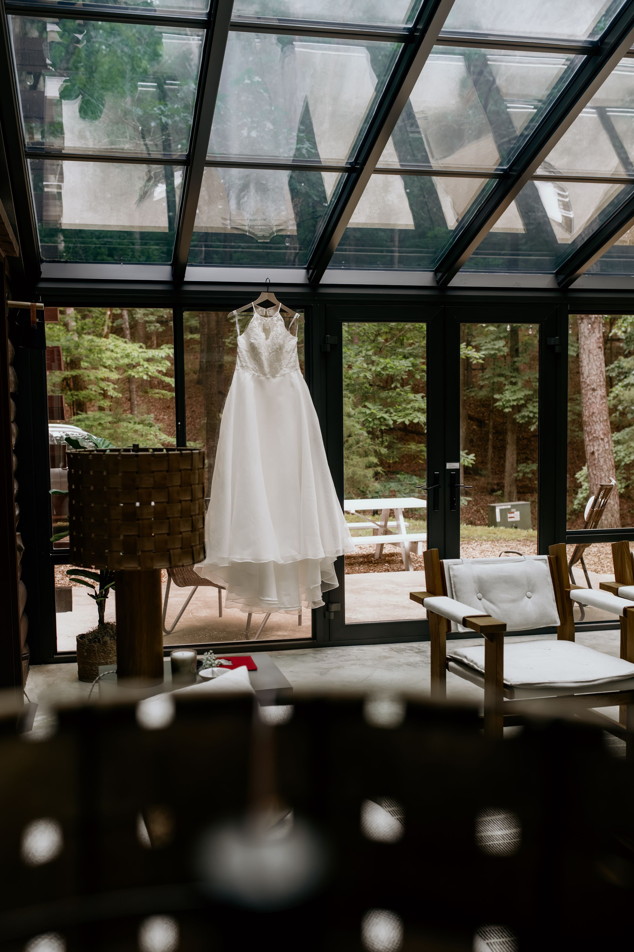 Wedding dress hangs in sunlit glass-ceiling room with mountain views.