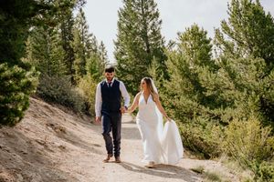 Wedding couple walking hand in hand through a pine forest path.