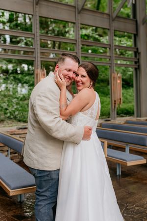 A couple sharing a joyful moment in a rustic indoor venue with wooden benches and glass windows.