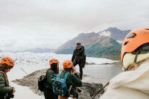 A group of hikers with orange helmets explore a snowy mountain glacier landscape.