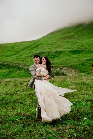 A couple twirling in a green mountain meadow with the bride's dress flowing in the wind.