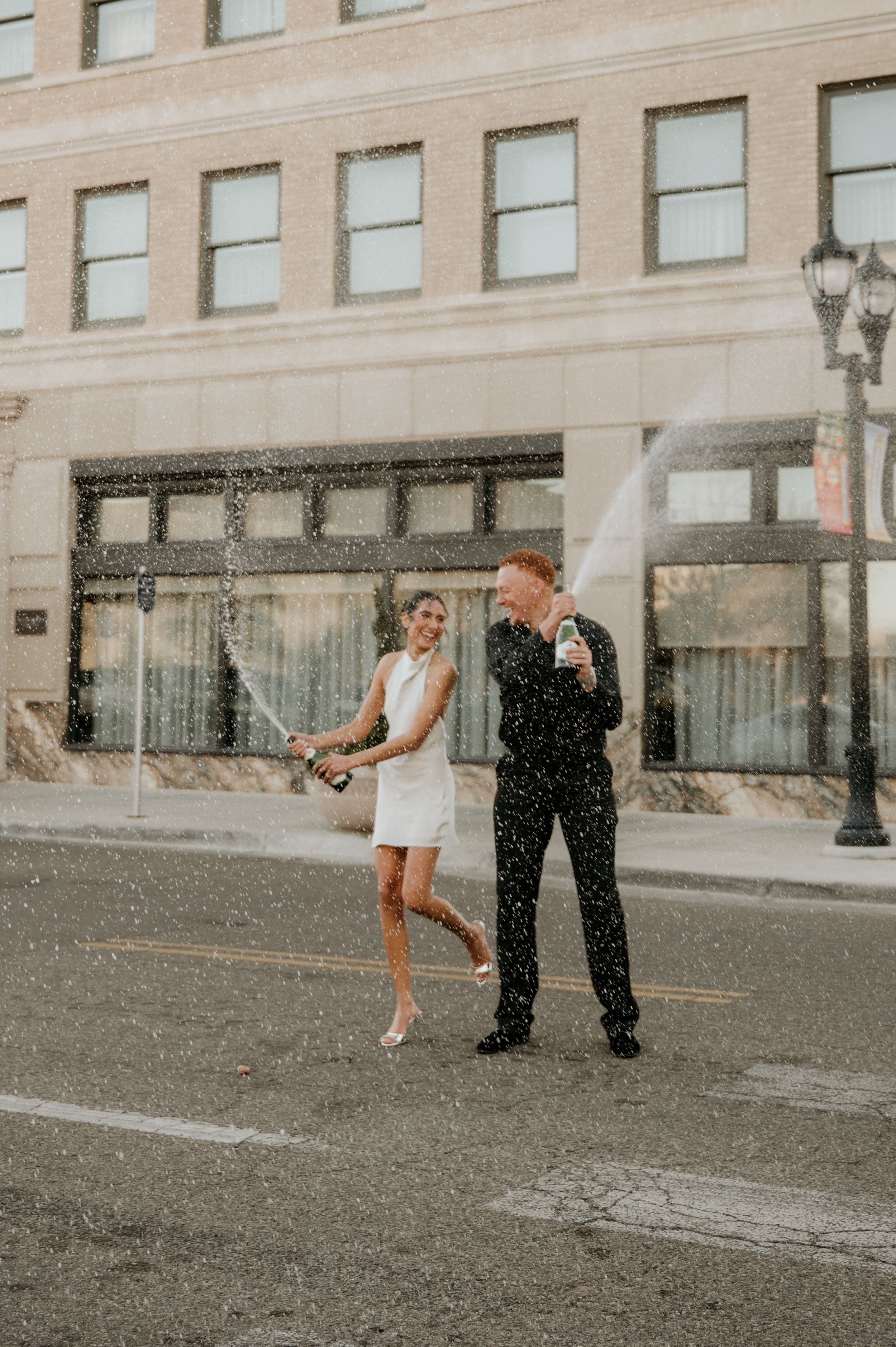 Playful wedding moment captured in front of a historic building with water splashing.