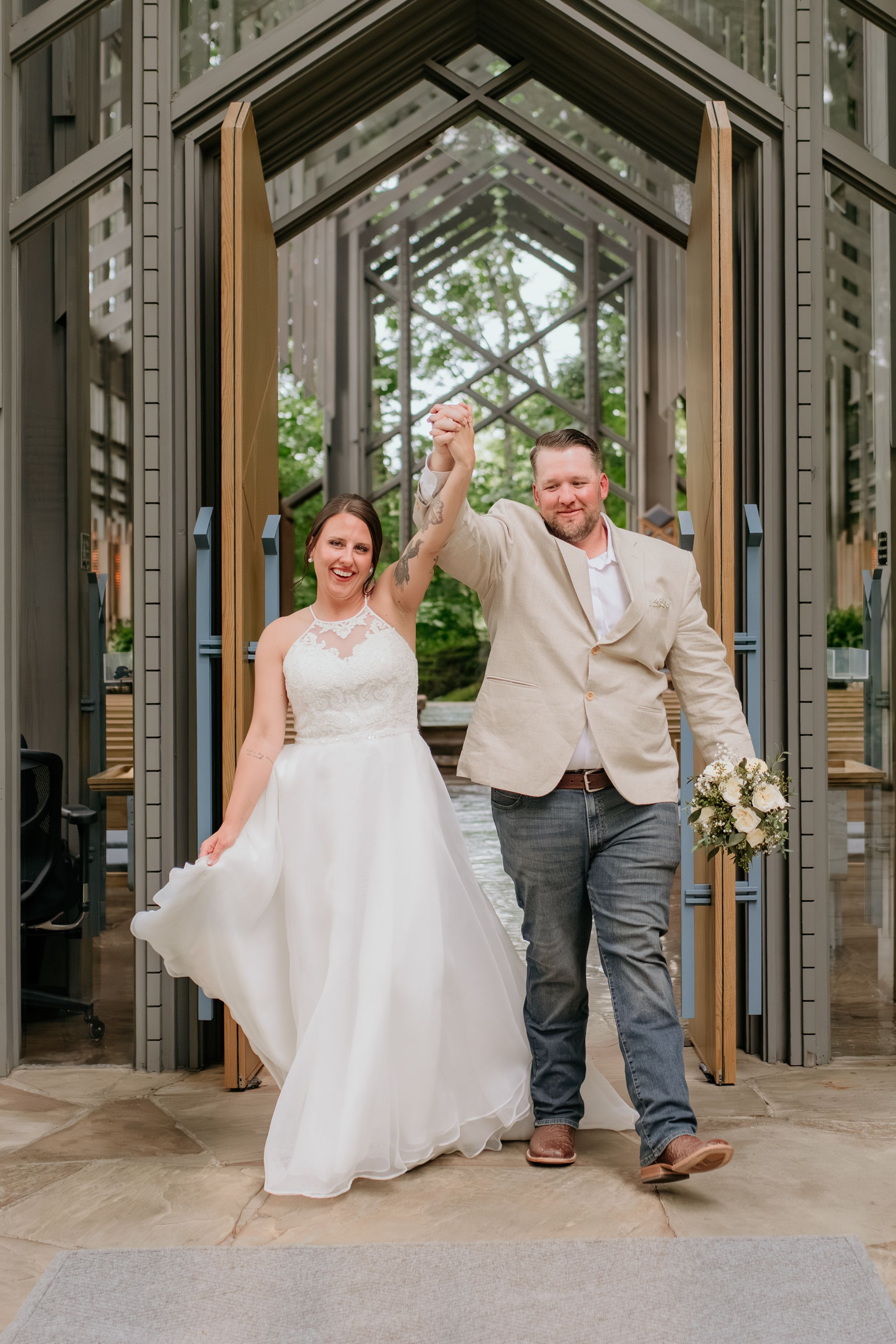 A couple dances playfully in a glass-walled chapel surrounded by greenery.