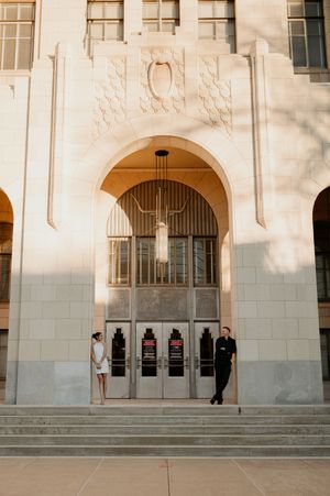A couple in wedding attire posing at the entrance of an art deco style building.